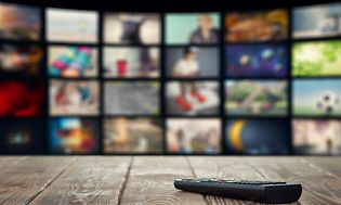 Böjd smart TV visar flera kanalval och i förgrunden ligger fjärrkontrollen på soffbordet