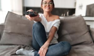 Kvinna sitter i soffa och riktar fjärrkontrollen mot Smart TV:n