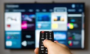 Hand håller fjärrkontroll riktad mot Smart-TV.