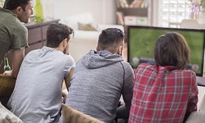 Fyra män sitter tätt ihop i en soffa och tittar på fotboll på TV. 