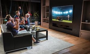 Ett gäng grabbar som samlats i soffan i ett vardagsrum för att se fotboll på en storbilds TV. Uppdukat med öl och snacks.  