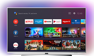 Smart TV på bordsstativ med silver ram och rosa bakgrundsljus, på skärmen visas olika appar och menyer.
