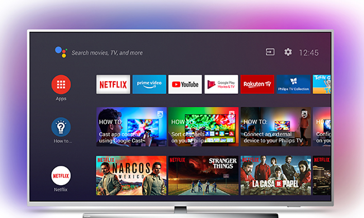 Smart TV på bordsstativ med silver ram och rosa bakgrundsljus, på skärmen visas olika appar och menyer.