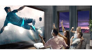 Ett gäng kompisar ser på fotboll med projektor i TV soffan och jublar 