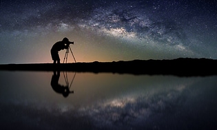 Profil siluett av en man med kameran och stativ under stjärnhimmel. 