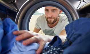 Bild från insidan av tvättmaskinen och ut på en man som håller på att plocka ur den rena tvätten, han ser nöjd ut.