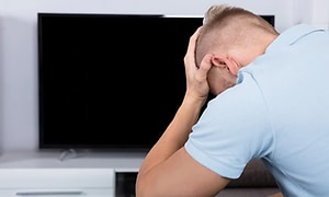 En man håller händerna I huvudet och ser frustrerad ut medan han sitter framför sin TV
