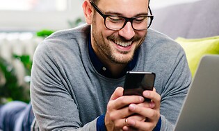 En man i glasögon ser på sin telefon och ler.