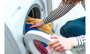 Närbild på tvättmaskin och händer som börjar ta ut ren tvätt i olika färger. 
