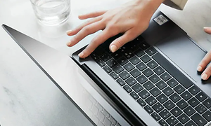 Ett finger hålls mot fingeravtrycksavläsaren på en laptop för att låsa upp den och logga in, längst upp i högra hörnet.