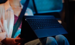 Kvinna sitter med en dator i knät, som hon har vikt så att tangentbordet är på andra sidan och inte används just nu. 