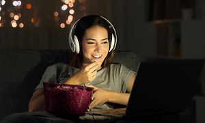 En tjej sitter i mörkret och ser på TV med hörlurar på och med popcornskålen i knät.