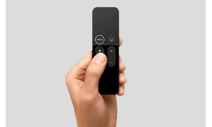 En hand håller upp en svart fjärrkontroll till Apple TV. Neutral grå bakgrund.