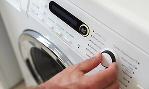 Närbild på knappar och menyn på en tvättmaskin, en hand ställer in vredet på rätt program. 
