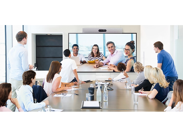 Flera människor i ett stort mötesrum deltar i ett videomöte med fyra personer som syns på en stor skärm. 