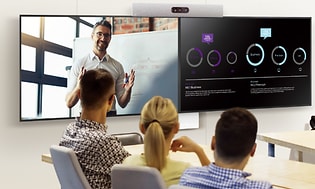 Tre personer sitter i ett konferensrum och samtalar med en person på videomöte, han syns på en stor skärm. 