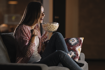 Hemmabio - En kvinna ser på film med inlevelse i soffan med popcorn.