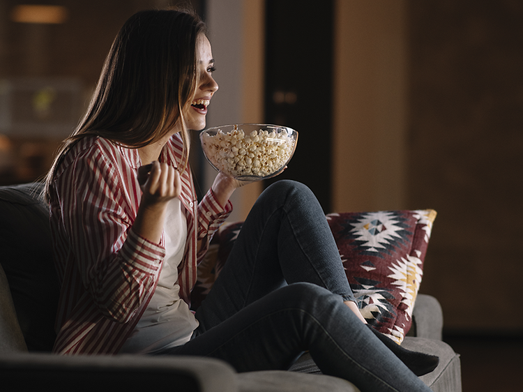 Hemmabio - En kvinna ser på film med inlevelse i soffan med popcorn.