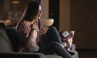 Hemmabio - En kvinna ser på film med inlevelse i soffan med popcorn.