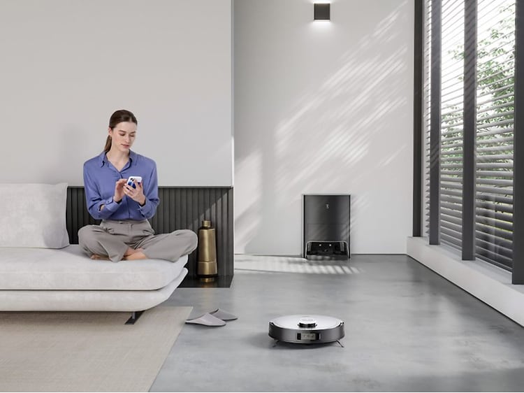 Deebot X1 städar golvet bredvid en kvinna på en soffa