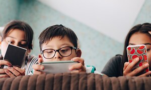 Vad ska du göra när mobilskärmen går sönder: Tre barn ligger i en säng och koller på sina mobiler.