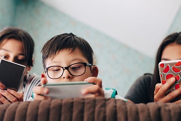 Vad ska du göra när mobilskärmen går sönder: Tre barn ligger i en säng och koller på sina mobiler.