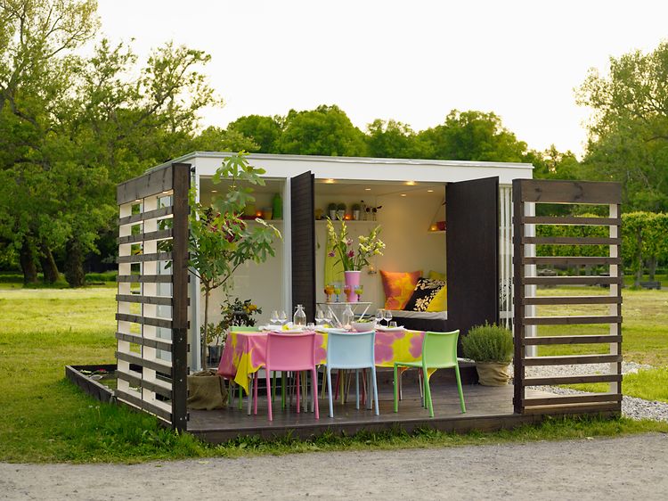 Uppdukat till fest på en paviljong i trädgården med färgglada stolar och en massa blommor. 