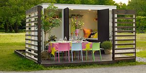 Uppdukat till fest på en paviljong i trädgården med färgglada stolar och en massa blommor. 