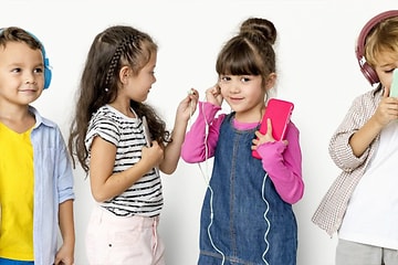 Fyra barn som står på rad framför en vit vägg, två har hörlurar på sig och de andra två delar på hörlurar. 
