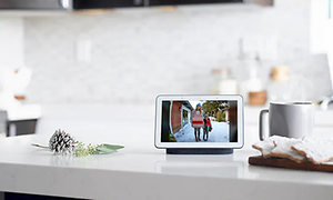 Google Nest Hub på en köksbänk visar övervakningskamera från entren där gäster närmar sig. En kopp kaffe står bredvid.