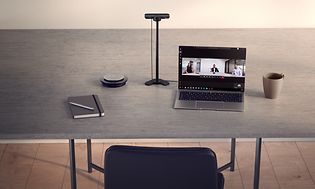 Hemmakontor med laptop, anteckningsbok och en kopp kaffe på ett grått bord. Teamsmöte på skärmen.
