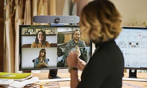 Kvinna med ryggen mot kameran deltar i videomöte med fyra andra på en datorskärm som deltar från olika platser.