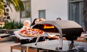 En pizza framför en pizzaugn med människor i bakgrunden