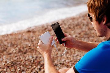 Man på strand som laddar sin smartphone med en powerbank