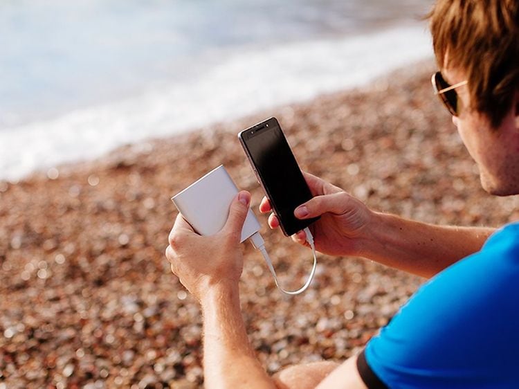 Man på strand som laddar sin smartphone med en powerbank