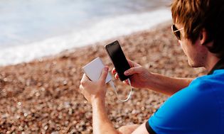 Man på strand som laddar sin smartphone med en powerbank