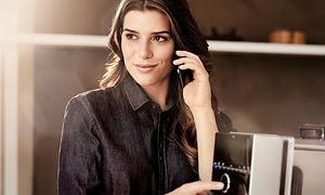 Kvinna som trycker på en knapp på Siemens kaffemaskin TI921309RW medan hon håller telefonen mot örat