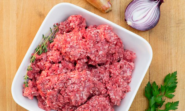 Malet kött i en vit skål på en köksbänk i trä, med lök och örter bredvid