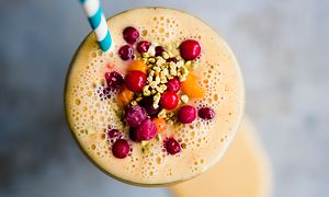 Orange smoothie i ett glas sett uppifrån med bär på toppen och ett sugrör