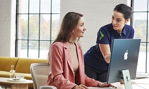 Kvinnlig anställd hos Elgiganten som hjälper kvinna att använda sin iMac