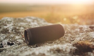 Portabel Bluetooth högtalare på en sten med natur i bakgrunden.