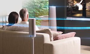 Par som tittar på TV i en ljus soffa i ett vardagsrum med flera högtalare och illustration av surroundljud