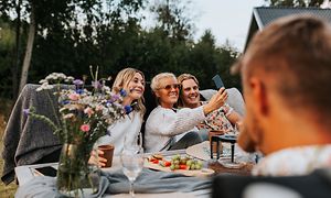 Två tjejer och en pojke tar en selfie i trädgården medan de sitter runt ett bord.