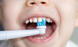 Närbild på ett litet barns mun och en eltandborste som borstar tänderna