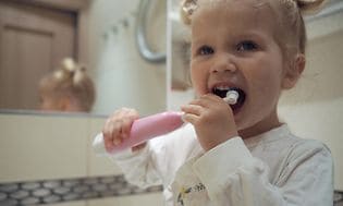 En glad liten flicka i ett badrum som borstar tänderna med en elektrisk tandborste
