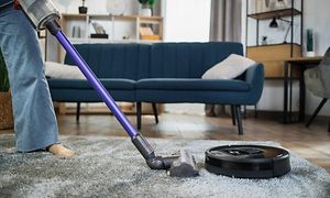 En person som dammsuger med en sladdlös dammsugare i ett vardagsrum bredvid en svart robotdammsugare