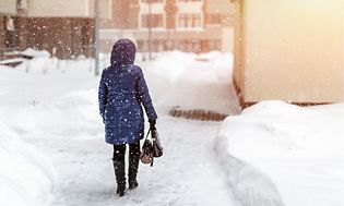 Uppvärmning: Kvinna som går genom stad när det snöar om vintern.