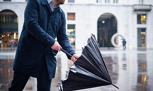 Uppvärmning: Regnig dag i stad och en affärsman öppnar sitt paraply.