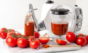 En Assistant-mixerkanna med tomatjuice med tomater runt den och en Ankarsum köksmaskin bakom den