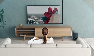 Kvinna i en ljus soffa tittar på Spiderman och runt och över TV:n är en illustration av en halvcirkel som visar hur ljudet når 